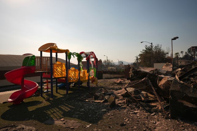 The sun shines over a playground. Its brightly coloured coverings have melted away and it is surrounded by burnt rubble 