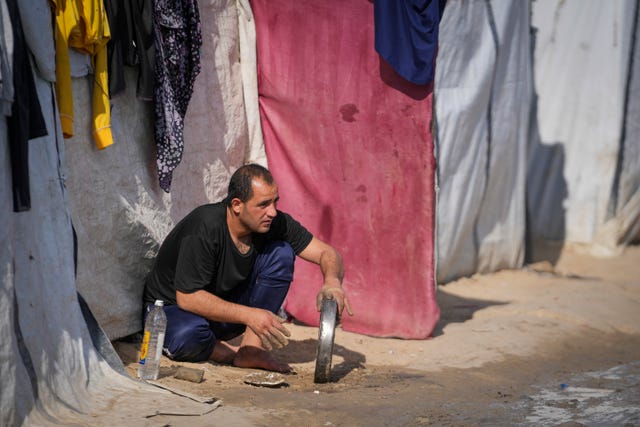 A man washes a tray outside a tent at a camp for displaced Palestinians in Deir al-Balah, central Gaza Strip 