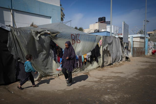 A woman and a child walk outside their tent at a camp for displaced Palestinians in Deir al-Balah, central Gaza Strip