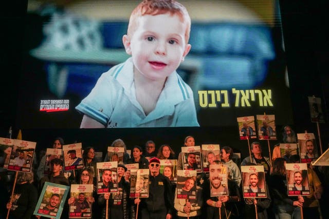 Demonstrators hold portraits of hostages held by Hamas in the Gaza Strip as a video featuring Ariel Bibas is played behind them