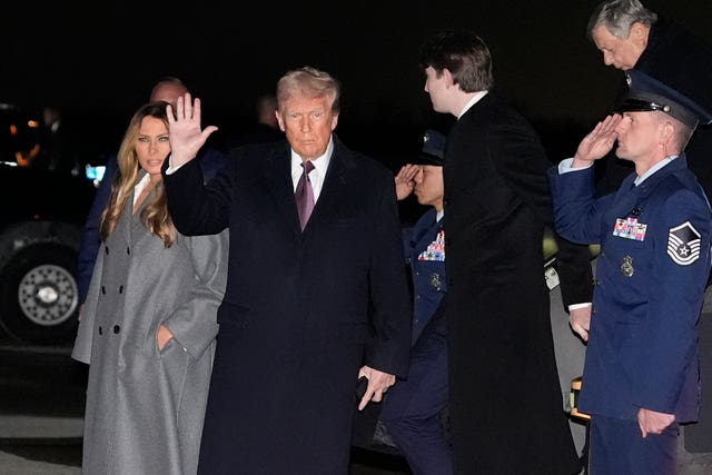 Donald Trump waving, next to wife Melania, while officials salute