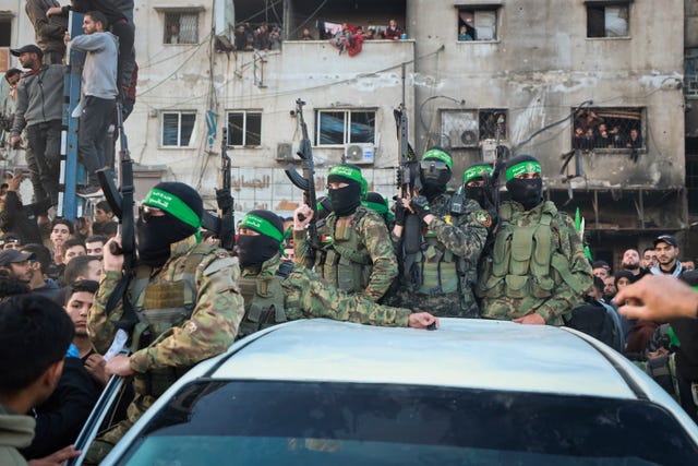 Fighters from the Qassam Brigades, the military wing of Hamas, stand atop a car in Gaza City as Red Cross vehicles manoeuvre to collect Israeli hostages released under a ceasefire agreement between Israel and Hamas