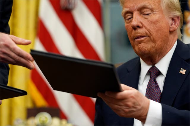 Donald Trump handing an executive order to an aide in the Oval Office of the White House