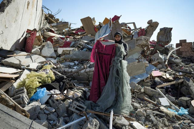 A woman holds up one of her dresses, salvaged from her devastated home in Rafah