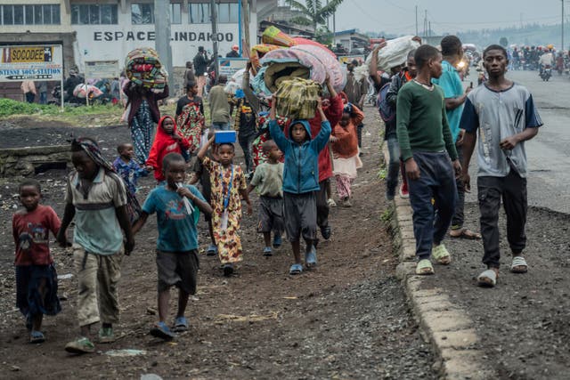 A crowd of people walk along the roadside, carrying their belongings