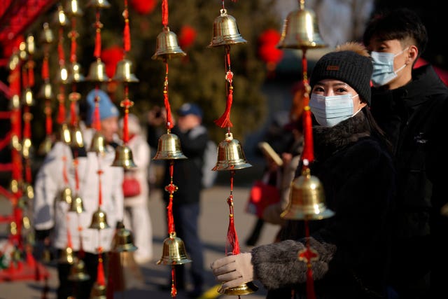 A woman touches bells for luck as people gather at the Ditan Temple Fair