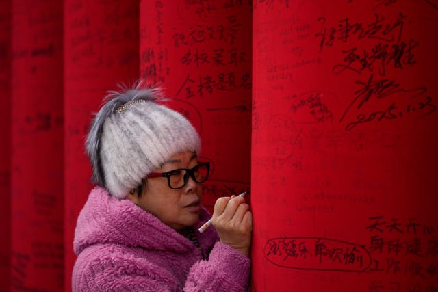 A woman writes wishes on a red cloth roll as people visit a temple fair held at the Dongyue Temple on the first day of the Chinese Lunar New Year in Beijing