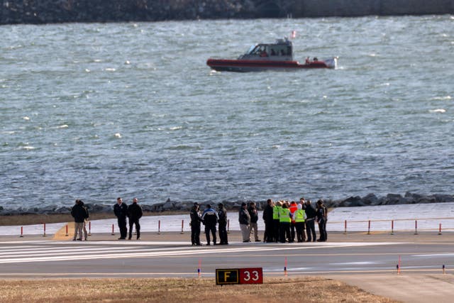 Officials gather at the end of a runway near the wreckage site in the Potomac River of a mid-air collision between an American Airlines jet and a Black Hawk helicopter