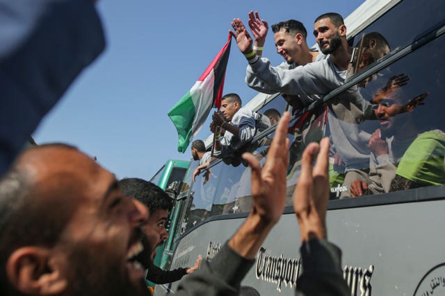 People cheer when a bus carrying men waving Palestinian flags arrives