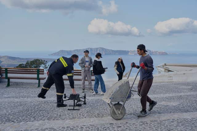 A firefighter controls a drone next to tourists after emergency crews were deployed to the island