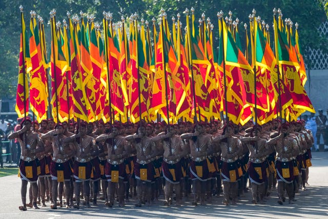 A group of men in traditional army uniform carry the national flag