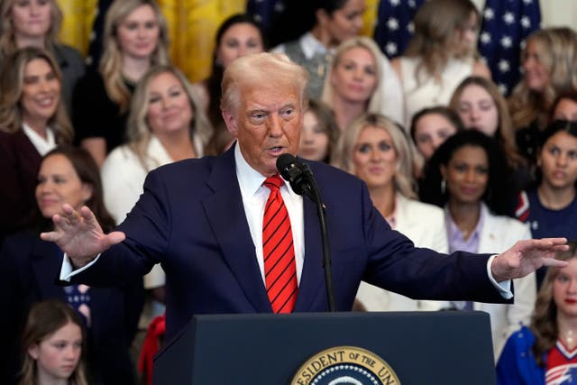 Donald Trump speaking from a presidential lectern, with an audience behind him