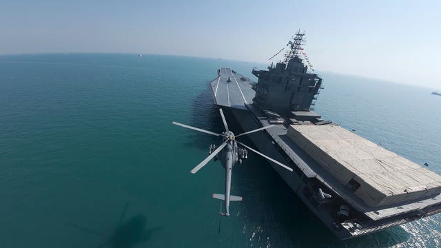 A helicopter flies over Iran’s first drone-carrier warship in the Persian Gulf 