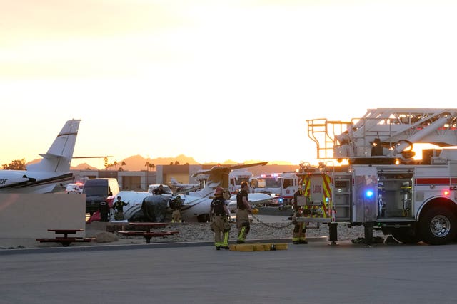 Members of the Scottsdale Fire Department stand near a crashed Learjet at Scottsdale Airport after it collided with a parked plane