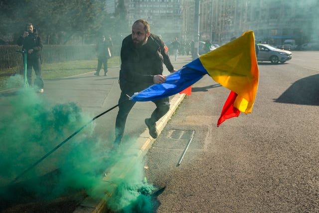 A man holding a Romanian flag runs after breaking through police lines in front of the government headquarters during a protest by supporters of Calin Georgescu