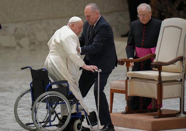 Pope Francis is helped by his assistant Piergiorgio Zanetti as he arrives for his weekly general audience in the Paul VI Hall at the Vatican on Wednesday