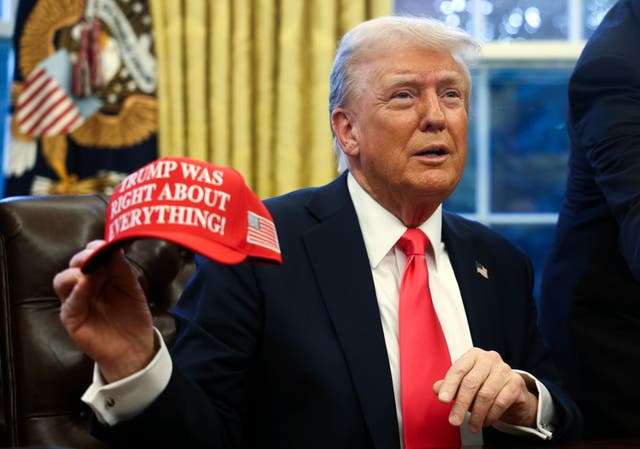 US President Donald Trump holds up a hat as he talks with reporters in the Oval Office at the White House in Washington