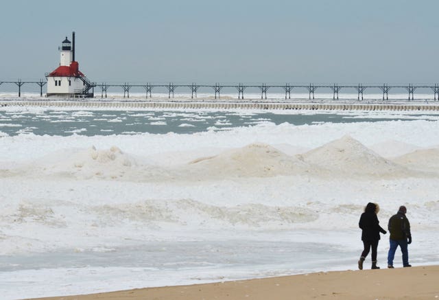 Two people walk along sand next to a build-up of sea ice