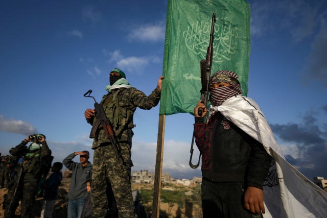 A boy holds a weapon as he stands next to a Hamas fighter standing in position ahead of handing over four bodies to the Red Cross in Khan Younis