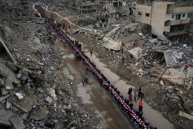 Palestinians sit at a large table surrounded by the rubble of destroyed homes and buildings as they gather for iftar, the fast-breaking meal, on the first day of Ramadan in Rafah