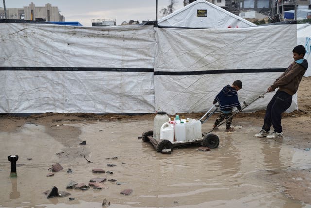 Children carrying water in plastic jerrycans at a tent camp for displaced Palestinians