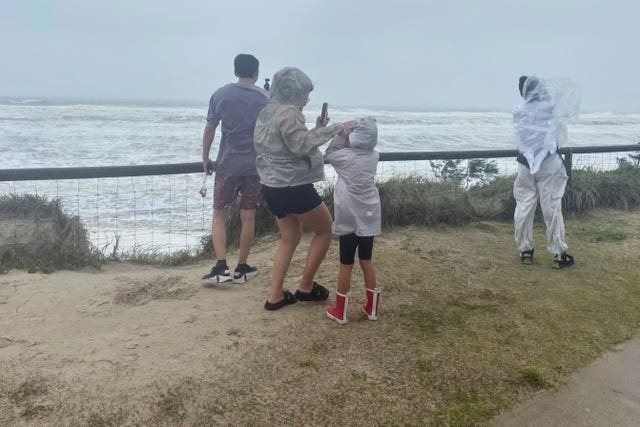 People stand at the beach in high winds as the remnants of cyclone Alfred arrives on the Gold Coast