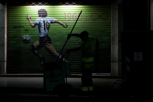 A refuse worker walks by a mural of late footballer Diego Maradona