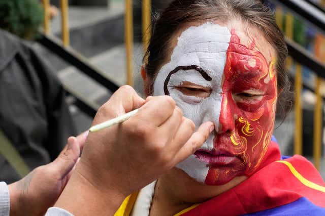 An exiled Tibetan gets her face painted before participating in a march 