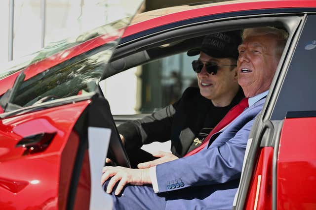 Donald Trump and Elon Musk speak to reporters as they sit in a red Model S Tesla vehicle