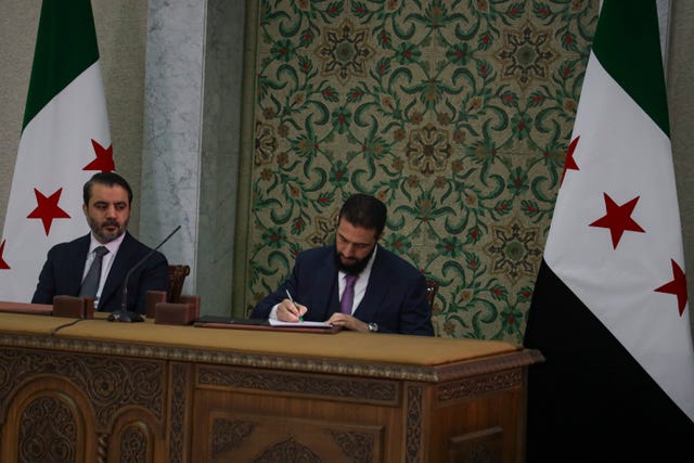 Syria’s interim president Ahmad Al-Sharaa, centre, signs a temporary constitution for the country  