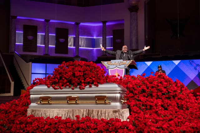 A silver and gold coffin surrounded by a sea of red roses 