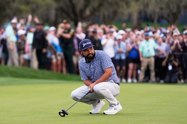 JJ Spaun crouches down holding his putter after a missed putt on the 18th green