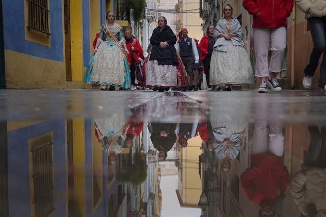 Women dressed in 18th and 19th-century clothing, known as falleras, reflected in a puddle of rainwater