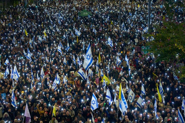 Thousands of people hold up phones with the flash on, signs and Israeli flags 