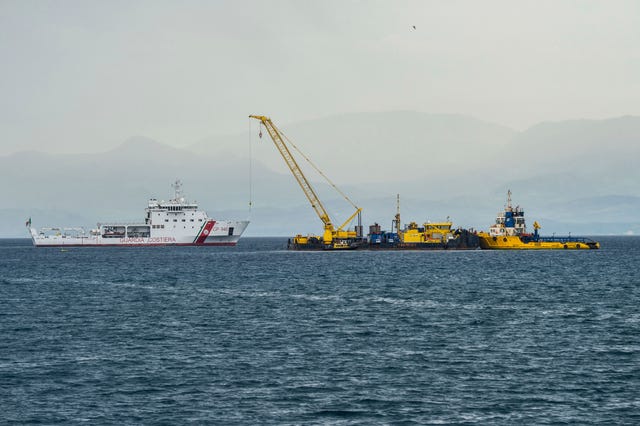An Italian coast guard patrol boat, left, assists a floating work barge