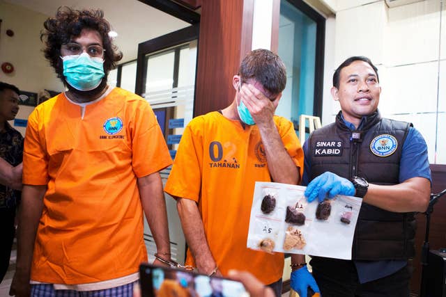 Australian national identified only as P.R., centre, and an Indian national identified as H.V., left, who were arrested for drug possession, react as a National Narcotics Agency officer shows evidence confiscated from them