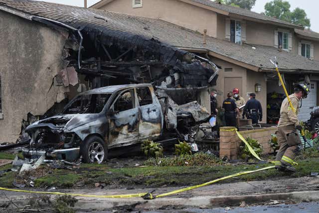 Charred remains of truck and house, firefighters are huddled together investigating