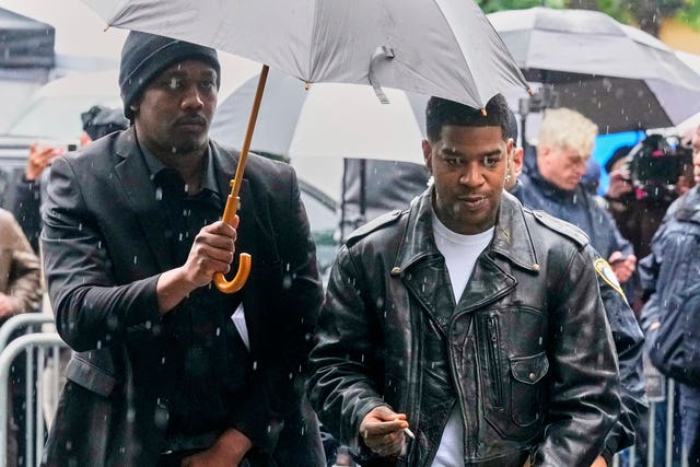 Two people walking, they're wearing leather jackets and holding big umbrellas