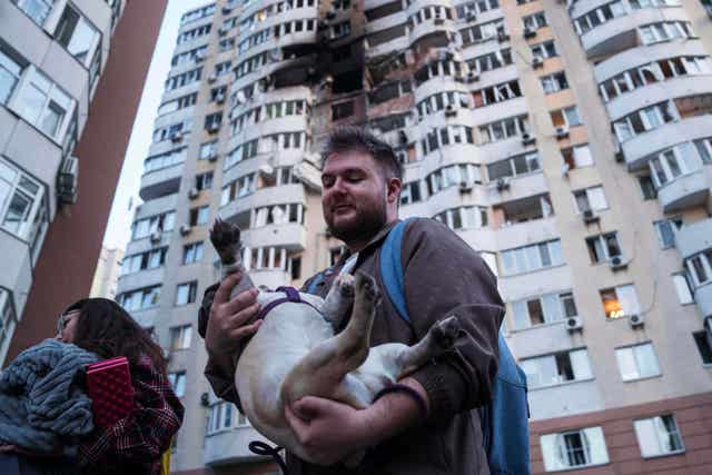 A man carries his dog in front of a residential multi-storey building 