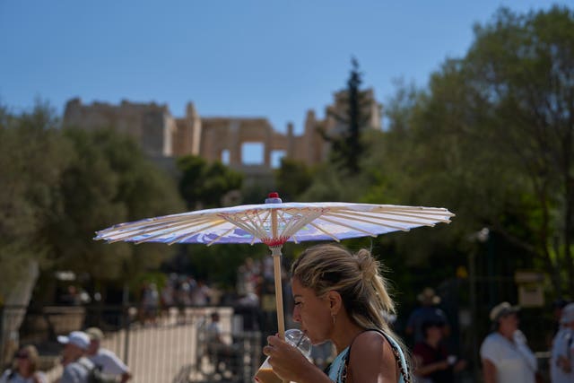 A tourist with an umbrella walks outside the Acropolis of Athens 