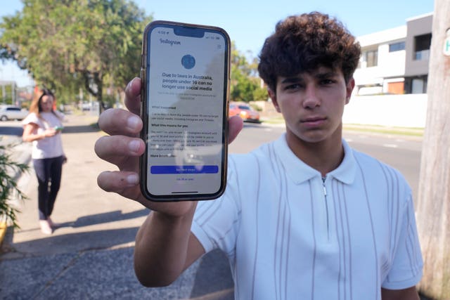 A boy holding up his phone displaying a warning that says he cannot access a social media site
