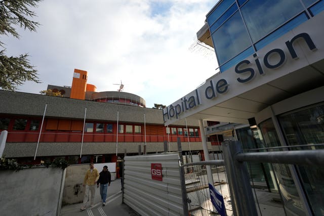 Two men walk outside a hospital as a helicopter takes off in Sion, Switzerland