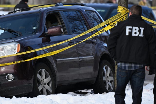 A bullet hole is seen in the vehicle's windshield as law enforcement officers work at the scene of the shooting
