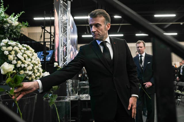 French President Emmanuel Macron places a white rose at a makeshift floral memorial