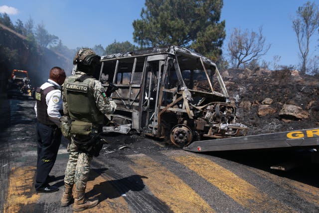A soldier stands guard near a charred vehicle 