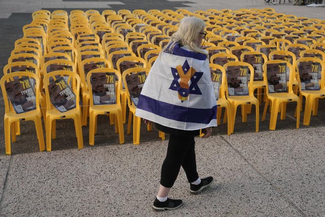 A woman walks past chairs with photos of Ran Gvili, the final hostage in Gaza who was killed while fighting Hamas militants during the October 7 2023 attack, on the same day his remains were recovered, in a plaza known as Hostages Square, in Tel Aviv, Israel 