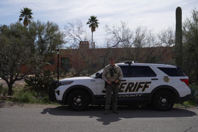A Pima County Sheriff’s Department member stands next to his vehicle in front of Nancy Guthrie’s home 
