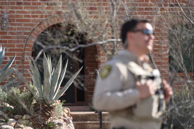 A member of the Pima County Sheriff’s Department stands in front of the front door of the house of Nancy Guthrie