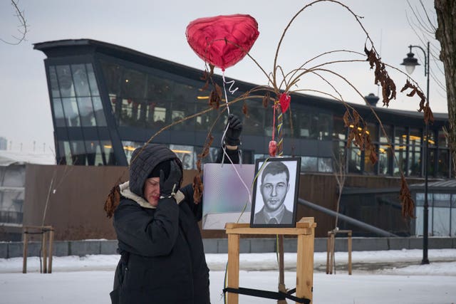 A woman weeping next to the photo of a fallen soldier, displayed under a love heart balloon
