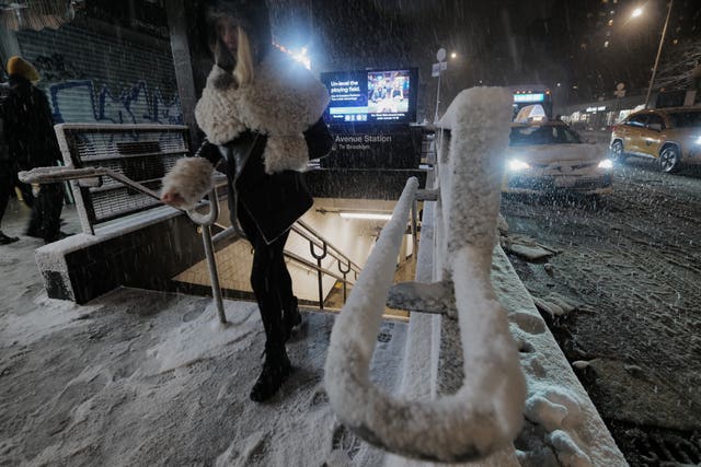 A passenger exits a subway station as snow falls in New York
